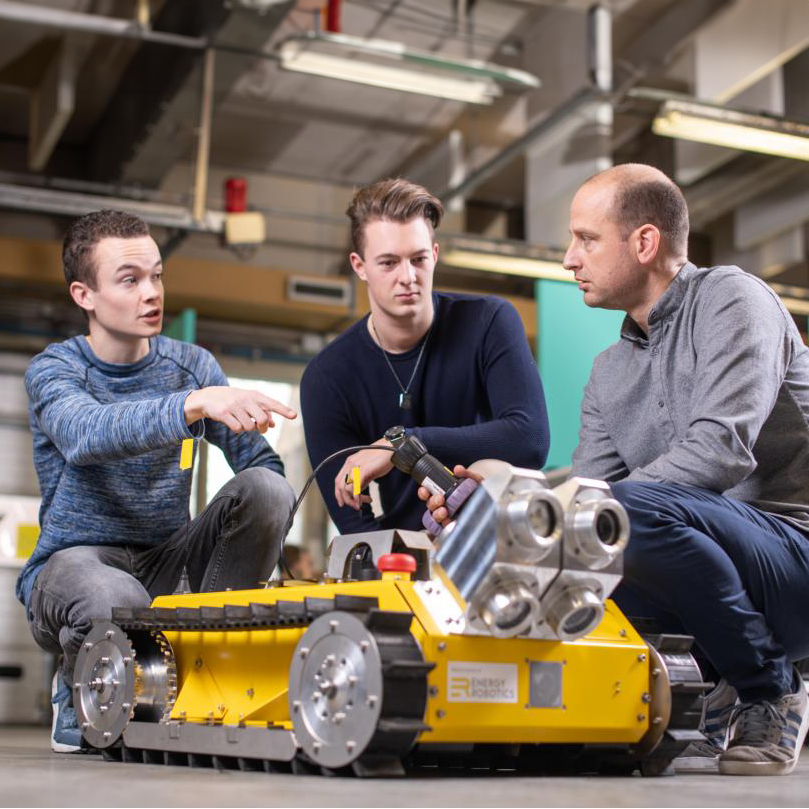 3 mannen zitten bij een gele robotkarretje
